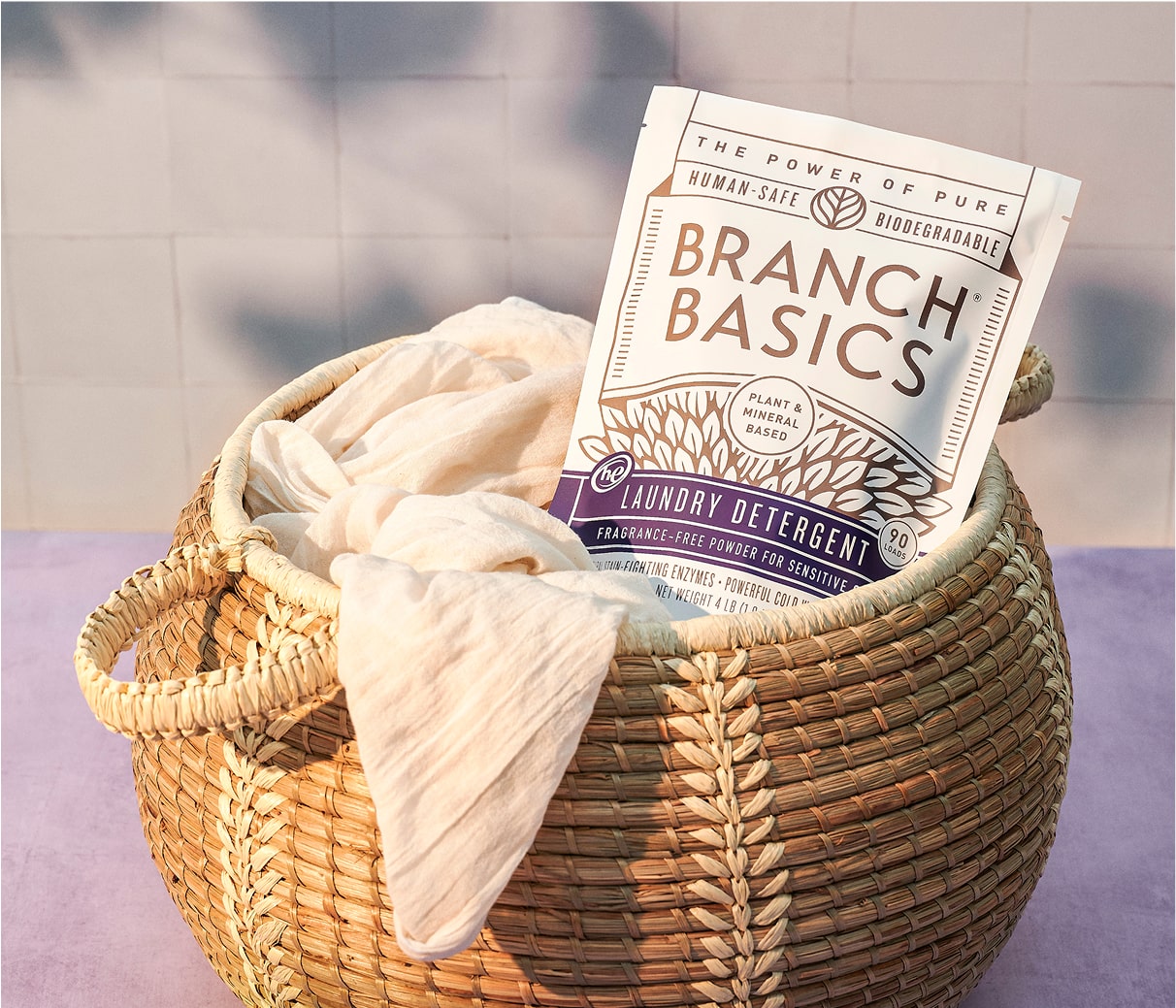 A pouch of Branch Basics Laundry Detergent tucked into a full laundry basket.